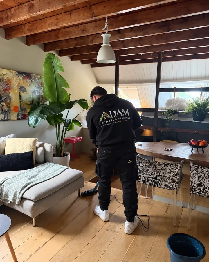 ADAM-medewerker stofzuigt een woonkamer, met het ADAM-logo op zijn trui