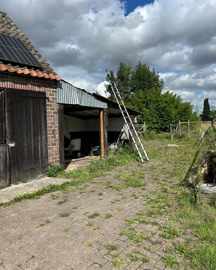 Medewerker aan het werk op het dak van een schuur, met een ladder tegen het gebouw